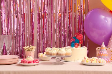 Farklı tatlılar ve dekorasyonlarla dolu bir masa. Pembe süs duvarına karşı.