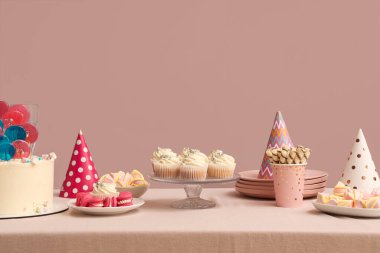 Doğum günü partisi için farklı şeker ve şapkalarla pembe duvarlı bir masa.