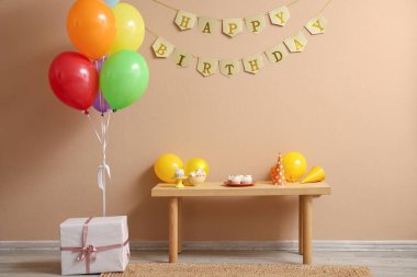 Farklı şekerlemeli masa, hediye kutusu ve bej duvarlı doğum günü partisi için balonlar