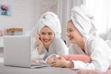 Evde dizüstü bilgisayarı olan bornozlu güzel, genç ve mutlu kız kardeşler.