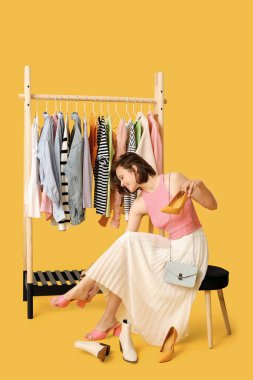 Farklı giysileri olan, sarı arka planda ayakkabı seçen güzel bir kadın.