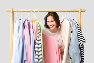 Beyaz arka planda farklı giysileri olan, rafların yanında güzel genç bir kadın.