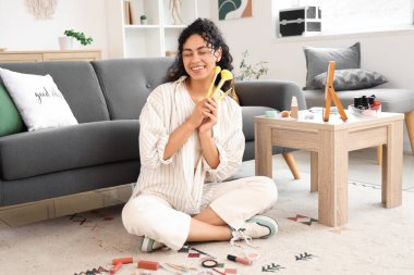 Makyaj fırçalarıyla evde makyaj yapan güzel, mutlu, Afro-Amerikalı bir kadın.