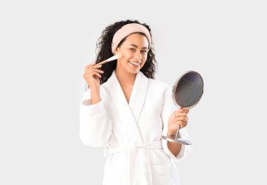 Beyaz arka planda ayna ve makyaj fırçası olan güzel, mutlu, Afro-Amerikan kadın.