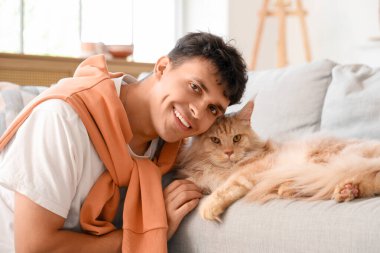 Evde sevimli Maine Coon kedisi olan yakışıklı, genç ve mutlu bir adam.