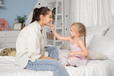 Little girl ill with chickenpox smearing her mother in bedroom clipart