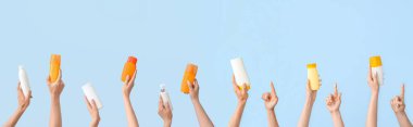 Açık mavi arkaplanda güneş kremi şişeleri olan bir sürü el