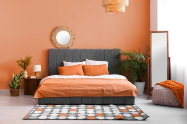 Portakal rengi duvarın yanında yatağı ve aynası olan modern yatak odası.