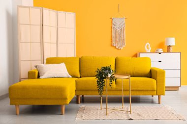 Sarı kanepe, oturma odasında masa ve katlanan ekran.