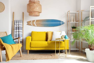 Açık oturma odasında sörf tahtası olan sarı kanepe.