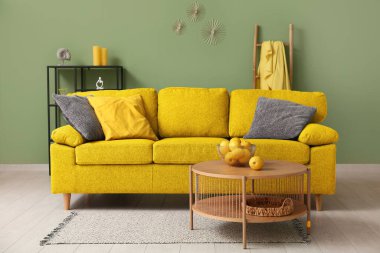 Oturma odasında yeşil duvarın yanında masalı sarı kanepe.