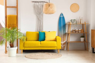 Sarı kanepe, sörf tahtası ve oturma odasındaki ışık duvarının yanında raflar.