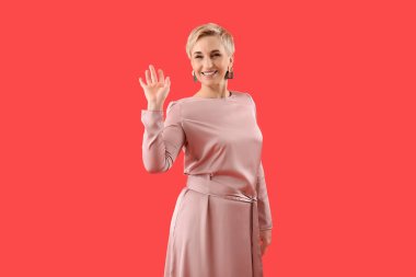 Kırmızı arka planda el sallayan şık, olgun bir kadın.
