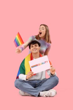 Kelime eşitliği ve pembe arka planda LGBT bayrakları olan genç bir çift ellerinde kağıt tutuyor.