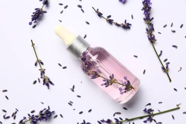 Beyaz zemin üzerinde gerekli yağ şişesi ve lavanta çiçekleri olan kompozisyon
