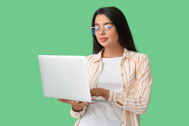 Genç bayan programcı yeşil arka planda dizüstü bilgisayarla çalışıyor.