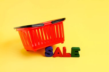 Sarı zemin üzerinde metin satışı olan küçük kırmızı alışveriş sepeti