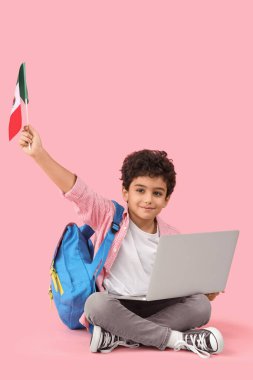 Pembe arka planda oturan, Meksika bayrağı ve dizüstü bilgisayarı olan küçük çocuk.