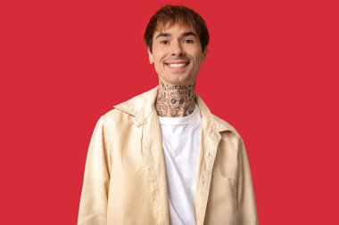 Kırmızı arka planda mutlu, yakışıklı, dövmeli adam.