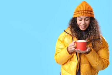 Mavi arka planda sıcak şarap bardağıyla güzel bir Afro-Amerikalı kadın.