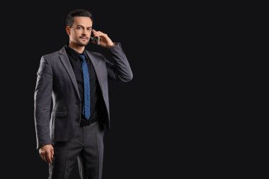 Koyu arkaplanda cep telefonuyla konuşan yakışıklı iş adamı