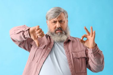 Olgun sakallı adam, mavi arka planda iyi ve kötü hareketler sergiliyor.