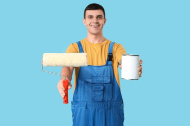 Mavi arka planda boya ve silindir kutusu olan genç bir ressam