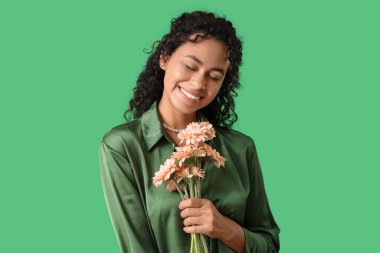 Yeşil arka planda bir buket Gerbera çiçeğiyle güzel bir Afro-Amerikalı kadın. Uluslararası Kadınlar Günü