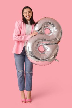 Pembe arka planda 8 şeklinde gümüş renkli balonu olan mutlu genç bir kadın. Uluslararası Kadınlar Günü