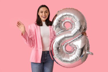 Pembe arka planda 8 şeklinde gümüş renkli balonu olan mutlu genç bir kadın. Uluslararası Kadınlar Günü