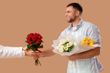 Erkek çiçekçi, bej arka plandaki müşteriye çiçek veriyor.