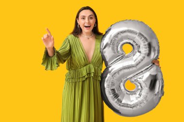 Sarı arka planda 8 şeklinde gümüş renkli hava balonu olan güzel genç bir kadın. Uluslararası Kadınlar Günü