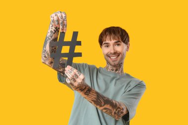 Sarı arka planda etiket sembolü olan havalı dövmeli genç adam.