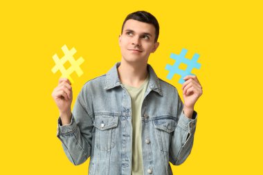 Sarı arka planda etiket sembolleri olan düşünceli genç bir adam.