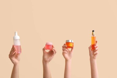 Kavanozlu ve şişeli kadın elleri bej arka planda farklı kozmetik ürünler