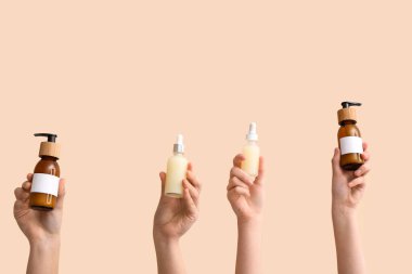 Bej arka planda farklı kozmetik ürünleri olan kadın elleri