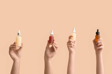 Bej arka planda farklı kozmetik yağı şişeleri olan kadın eller.