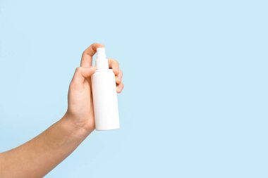 Mavi arka planda bir şişe kozmetik spreyi olan kadın eli.