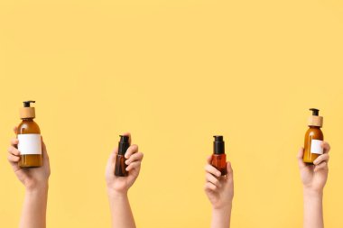 Sarı arka planda farklı kozmetik ürünleri olan kadın elleri