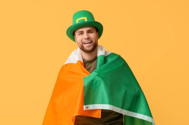 Sarı arka planda İrlanda bayrağı olan cüce şapkalı mutlu genç adam. Aziz Patrick Günü kutlaması