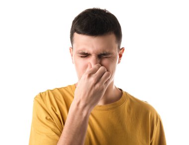 Beyaz arka plandaki kötü koku yüzünden burnunu çimdikleyen yakışıklı genç adam.