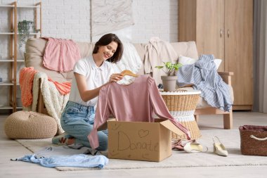 Genç ve güzel bir kadın, evdeki bağış kutusunda giysilerini paketliyor.
