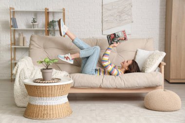 Genç, güzel bir kadın dergi okuyor ve oturma odasındaki kanepede dinleniyor.