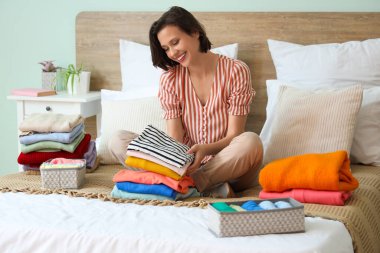 Evde yatağında farklı giysileri olan genç ve güzel bir kadın.