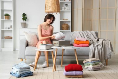 Genç ve güzel bir kadın evdeki kanepede elbiselerini katlıyor.