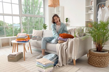 Genç kadın farklı giysiler katlıyor ve evdeki kanepede oturuyor.