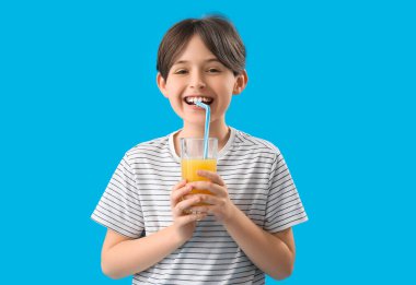 Küçük çocuk mavi arka planda portakal suyu içiyor.