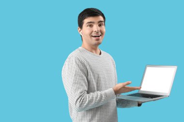 Mavi arka planda dizüstü bilgisayarı olan kulaklıklı bir erkek programcı.