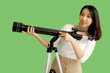 Genç Asyalı kadın yeşil arka planda teleskop kullanıyor.
