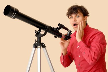 Bej arka planda teleskopu olan şaşırmış genç bir adam.